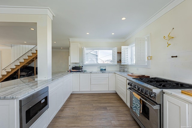 kitchen with light stone countertops, appliances with stainless steel finishes, ornamental molding, white cabinets, and light hardwood / wood-style floors