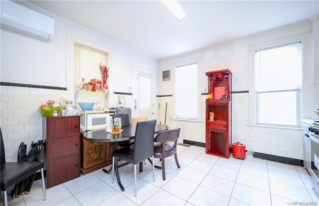 tiled dining room with a wall mounted AC, crown molding, a healthy amount of sunlight, and tile walls