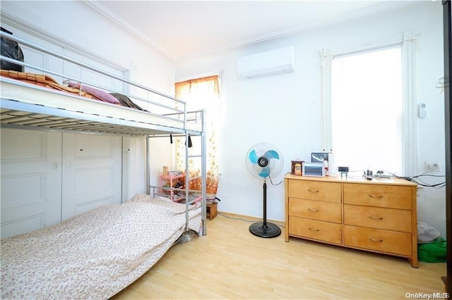 bedroom featuring a wall unit AC, crown molding, and light wood-type flooring