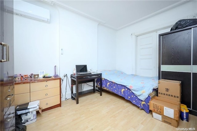 bedroom with ornamental molding, a wall mounted air conditioner, and hardwood / wood-style flooring