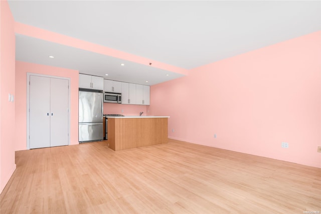 kitchen with white cabinetry, a center island, stainless steel appliances, and light wood-type flooring