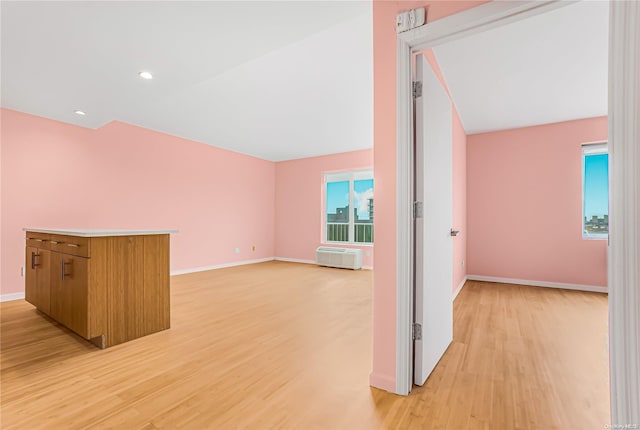 corridor with light hardwood / wood-style floors, vaulted ceiling, and an AC wall unit