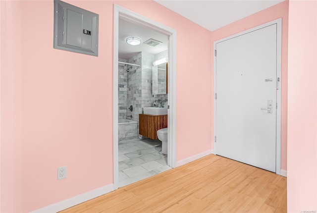 hallway with wood-type flooring, electric panel, and sink