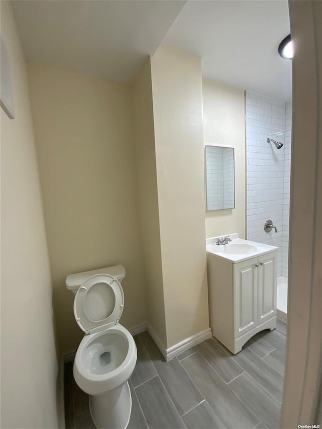 bathroom featuring a tile shower, vanity, and toilet