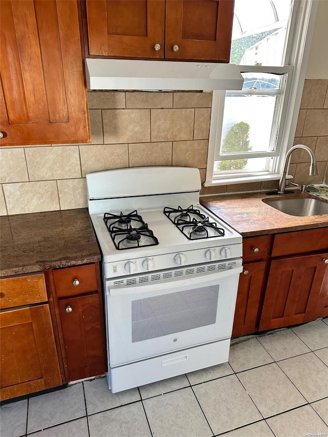 kitchen with light tile patterned floors, tasteful backsplash, white gas stove, and sink