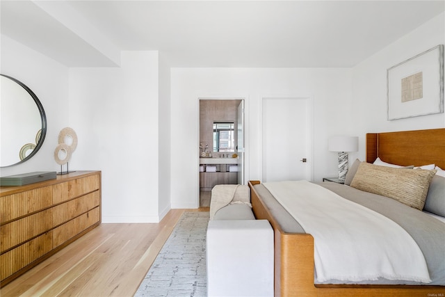 bedroom featuring ensuite bathroom, light wood-type flooring, and baseboards