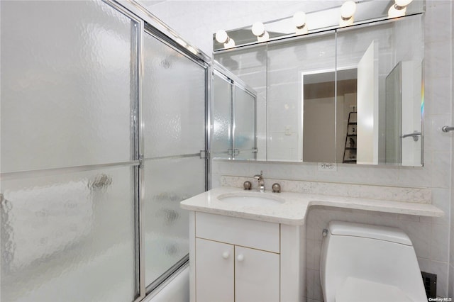 full bathroom featuring vanity, bath / shower combo with glass door, tile walls, and toilet