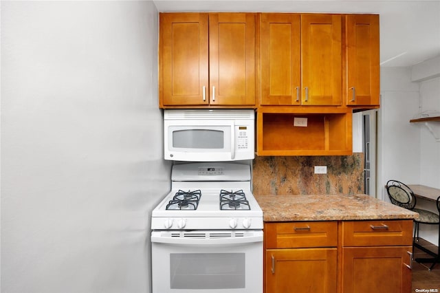 kitchen featuring decorative backsplash, light stone counters, and white appliances