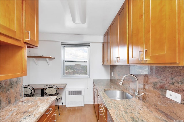 kitchen with light wood-type flooring, backsplash, light stone counters, and sink