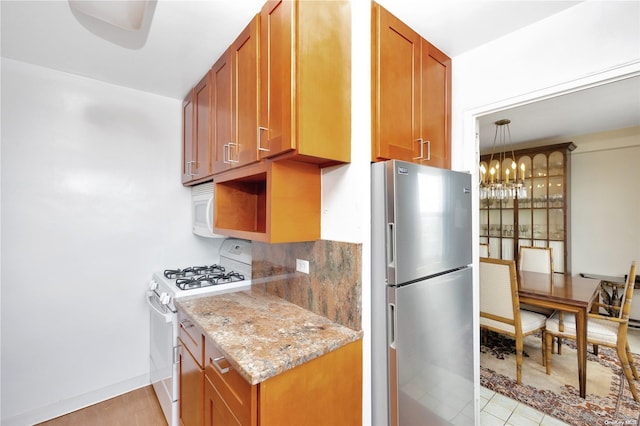 kitchen with white gas stove, light stone counters, light hardwood / wood-style flooring, backsplash, and stainless steel fridge