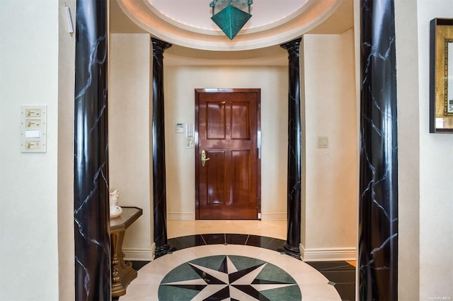 corridor featuring baseboards, a raised ceiling, tile patterned floors, and ornate columns