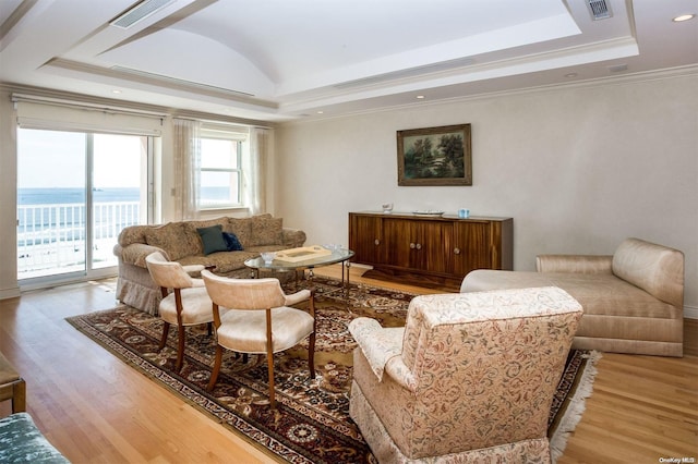 living room featuring a raised ceiling, a water view, ornamental molding, and hardwood / wood-style floors