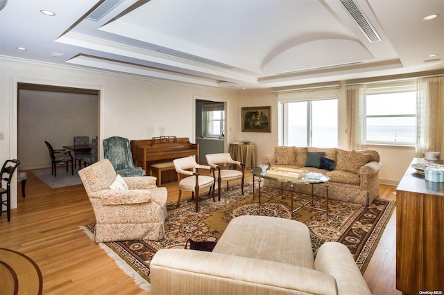 living room with wood-type flooring, a raised ceiling, and crown molding