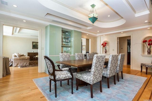 dining room with a tray ceiling, crown molding, and light hardwood / wood-style floors