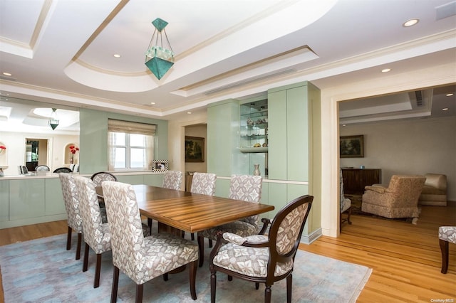 dining space featuring a raised ceiling, light wood-type flooring, and crown molding