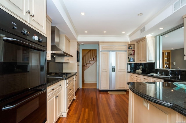 kitchen featuring black appliances, wall chimney exhaust hood, dark hardwood / wood-style floors, dark stone countertops, and ornamental molding