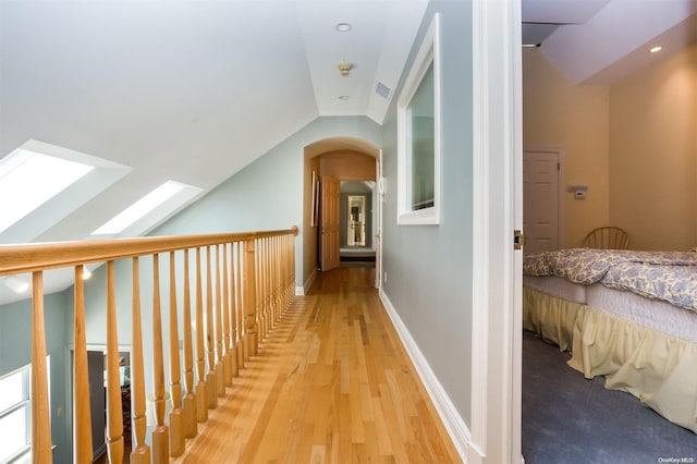 corridor with lofted ceiling with skylight and light hardwood / wood-style floors