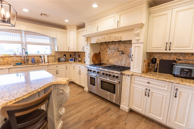 kitchen with range with two ovens, sink, decorative backsplash, light stone countertops, and light wood-type flooring