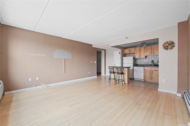 kitchen featuring white appliances, light hardwood / wood-style flooring, decorative backsplash, a textured ceiling, and a kitchen bar