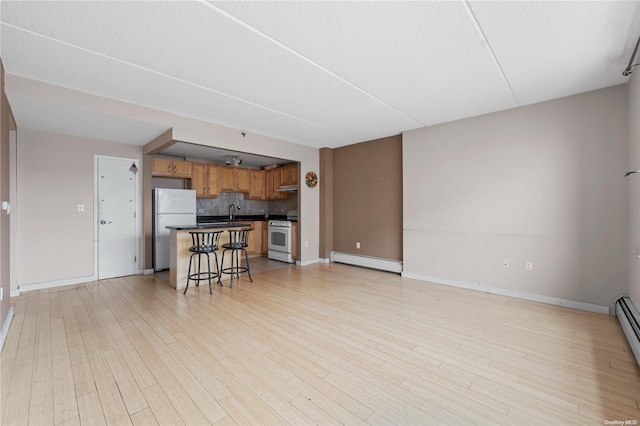 kitchen with white appliances, a kitchen breakfast bar, light hardwood / wood-style flooring, a baseboard radiator, and a kitchen island