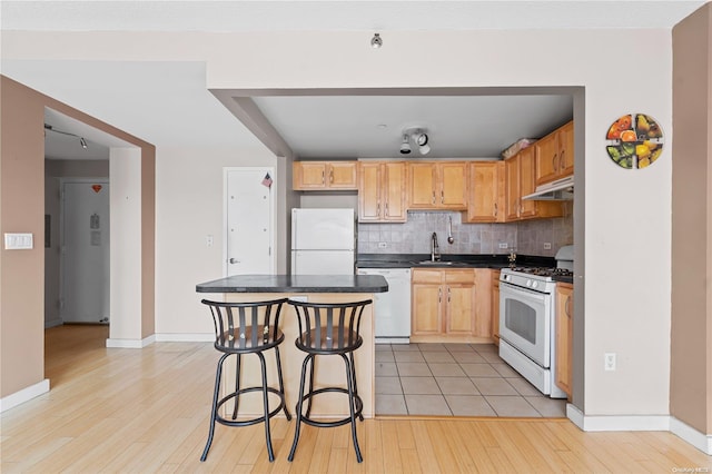 kitchen with decorative backsplash, white appliances, sink, and light hardwood / wood-style flooring