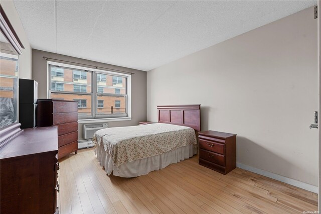 bedroom featuring a wall mounted AC, light hardwood / wood-style flooring, and a textured ceiling