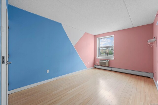 bonus room with a wall unit AC, light hardwood / wood-style flooring, a textured ceiling, and a baseboard heating unit