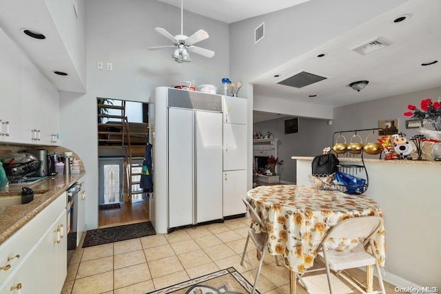 kitchen featuring ceiling fan, dishwasher, a high ceiling, light tile patterned flooring, and white cabinets