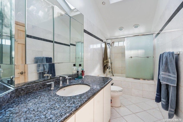 full bathroom with tile patterned floors, bath / shower combo with glass door, toilet, vaulted ceiling with skylight, and vanity