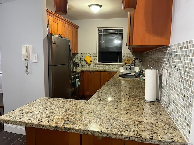 kitchen with stainless steel refrigerator, sink, kitchen peninsula, decorative backsplash, and black range