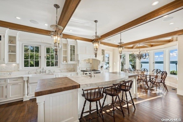 kitchen with white cabinetry, a center island, dark wood-type flooring, hanging light fixtures, and a water view