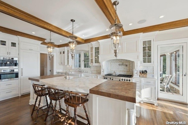 kitchen with backsplash, decorative light fixtures, white cabinetry, and a kitchen island with sink