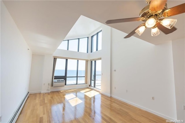 interior space featuring a wall mounted AC, baseboard heating, ceiling fan, a water view, and light hardwood / wood-style floors