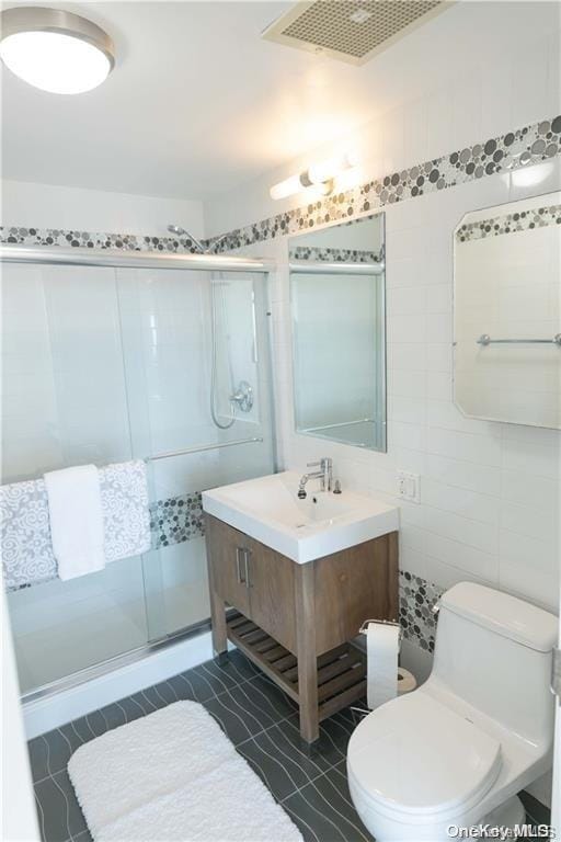 bathroom with walk in shower, vanity, tile walls, and toilet