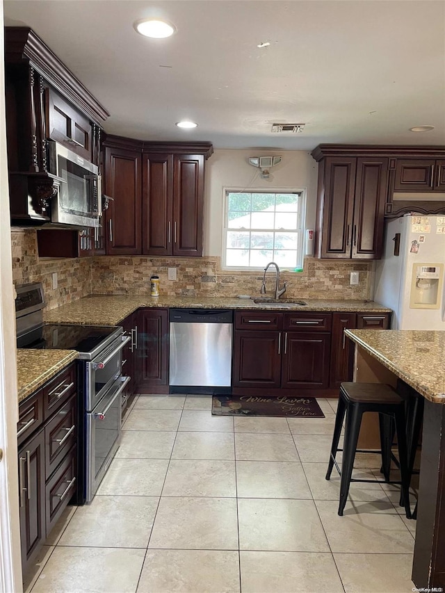 kitchen with sink, light tile patterned floors, light stone counters, dark brown cabinetry, and stainless steel appliances