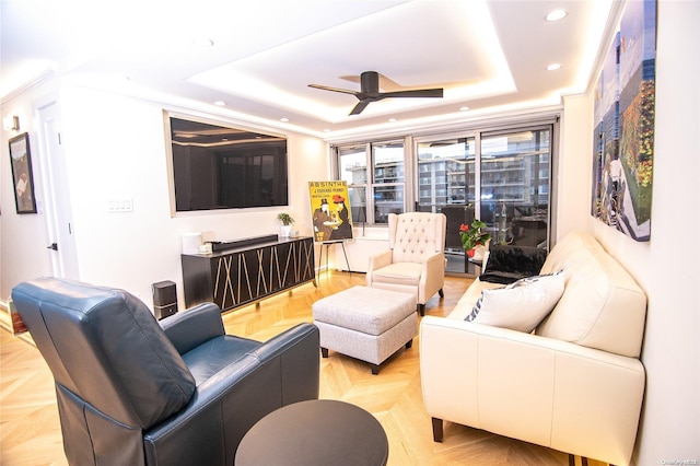 living room with ceiling fan, ornamental molding, a tray ceiling, and light parquet floors