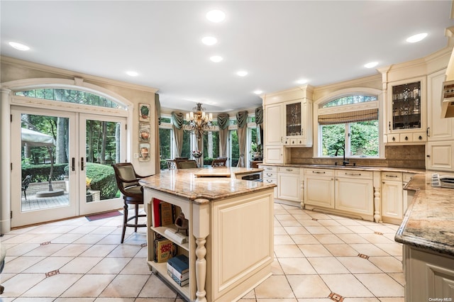 kitchen featuring french doors, light stone counters, cream cabinets, decorative backsplash, and a kitchen island