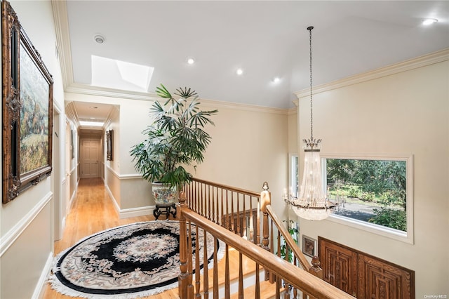 hall with a notable chandelier, light hardwood / wood-style floors, ornamental molding, and vaulted ceiling