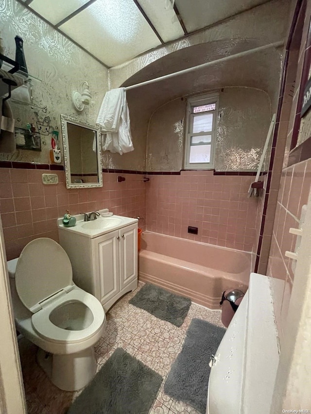 full bathroom featuring tiled shower / bath combo, toilet, tile walls, and vanity