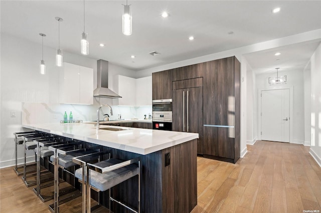 kitchen featuring hanging light fixtures, a breakfast bar, white cabinets, and wall chimney exhaust hood