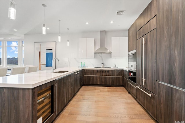 kitchen with pendant lighting, sink, white cabinetry, beverage cooler, and wall chimney exhaust hood