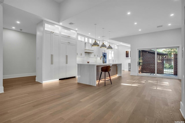 kitchen with premium range hood, decorative light fixtures, a center island with sink, light hardwood / wood-style flooring, and white cabinetry