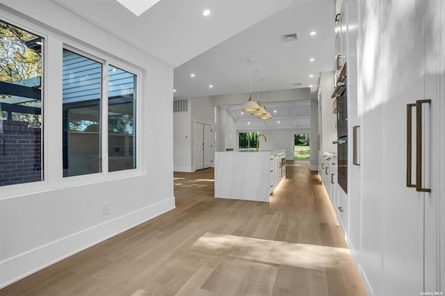 interior space with sink, pendant lighting, light hardwood / wood-style floors, white cabinetry, and an island with sink