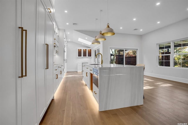 kitchen featuring white cabinets, decorative light fixtures, a center island with sink, and a wealth of natural light