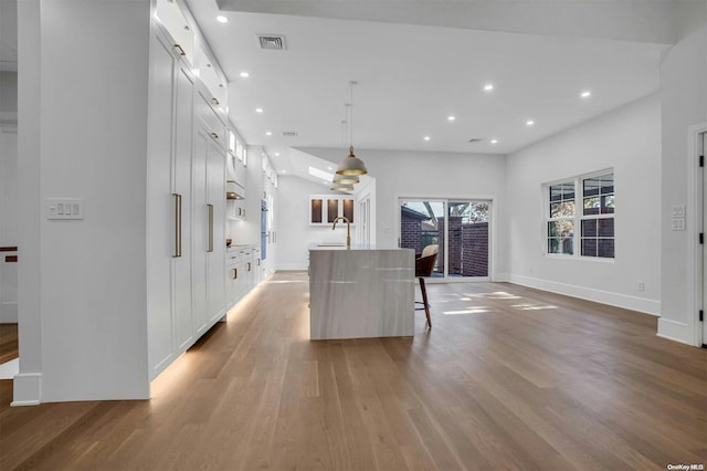 kitchen featuring a kitchen island with sink, a breakfast bar, wood-type flooring, and decorative light fixtures