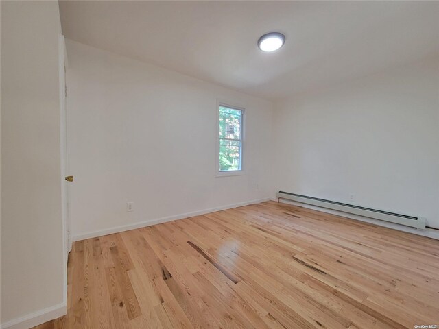 unfurnished room featuring a baseboard heating unit, baseboards, and wood finished floors