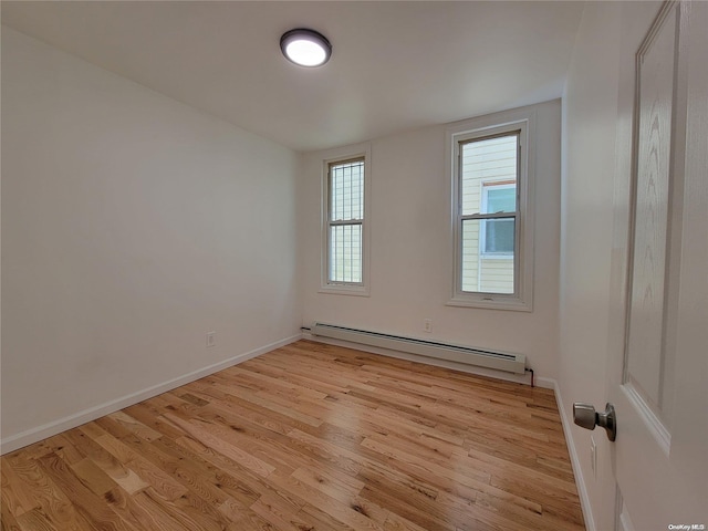 spare room with baseboards, light wood-style floors, and a baseboard radiator