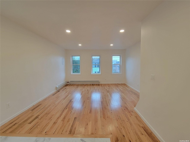 empty room with a baseboard heating unit, recessed lighting, baseboards, and light wood finished floors