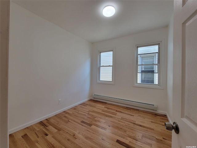 empty room featuring light wood-style flooring, a baseboard heating unit, and baseboards