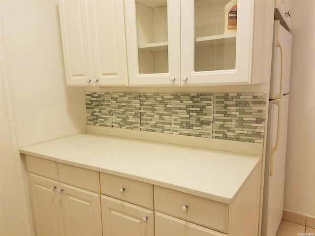 kitchen featuring white refrigerator, tile patterned flooring, light stone countertops, tasteful backsplash, and white cabinetry